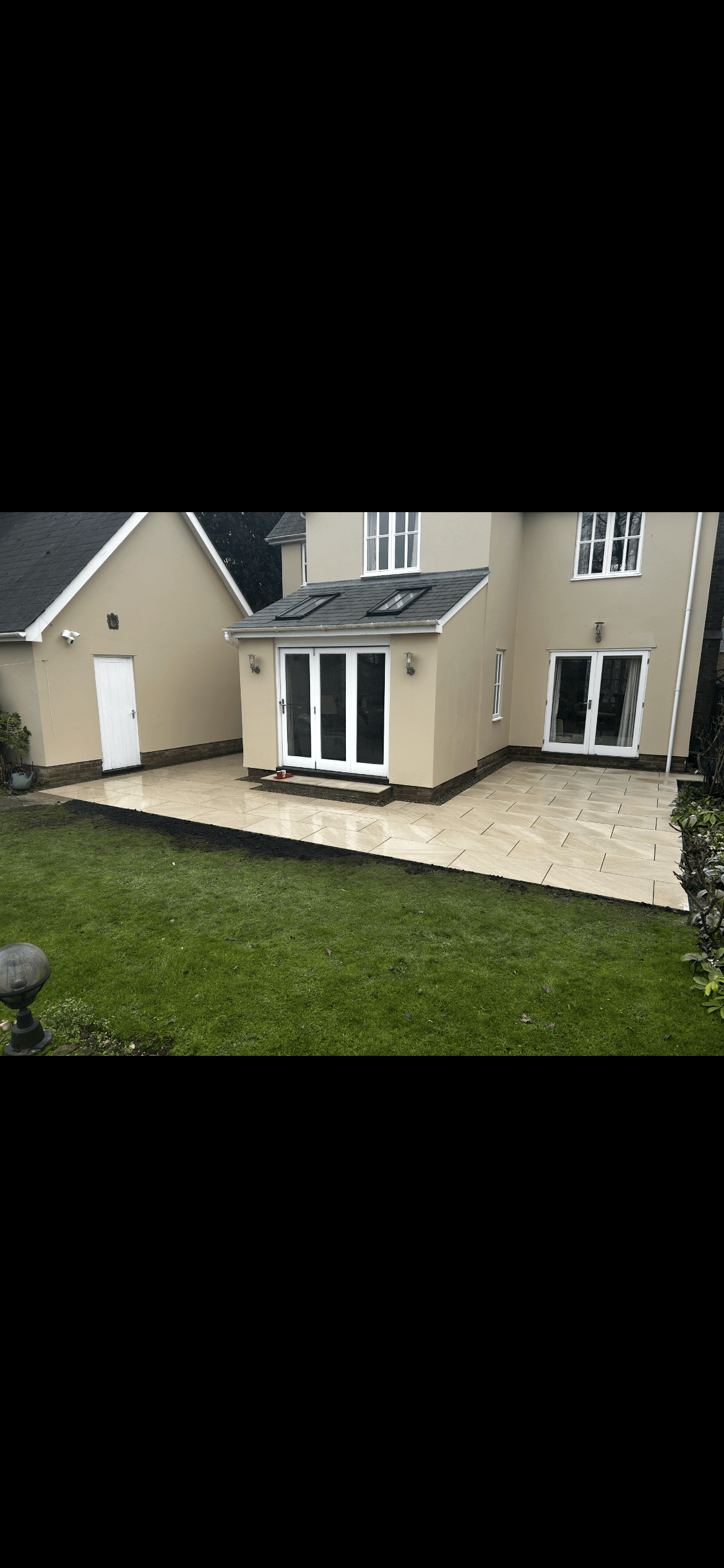 Modern tan house featuring white French doors, a light stone patio, and green lawn.